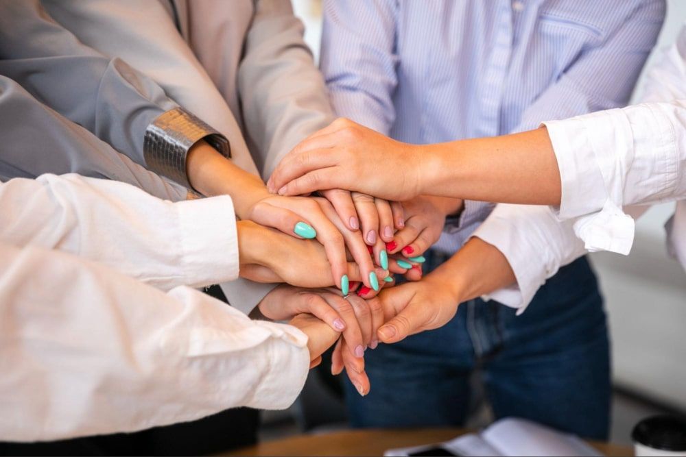 Women celebrating with hands stacked for culture of recognition in the workplace