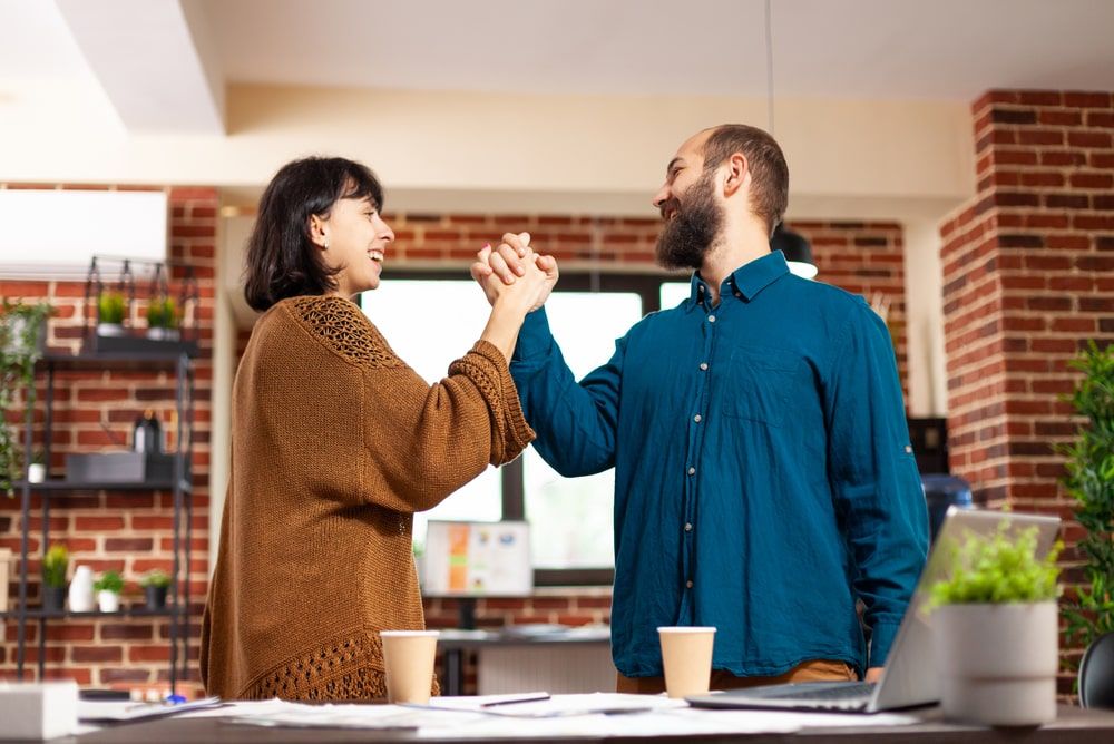 Manager and employee celebrating project completion in a startup office, fused with closing sales techniques, embodying effective strategies and shared success and preparing to give company gifts to employees