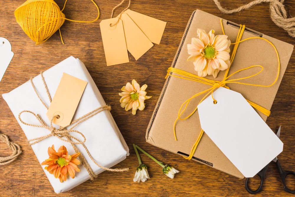 Two bulk gifts for employees wrapped and tied with tag strings and beautiful flowers on a wooden surface.