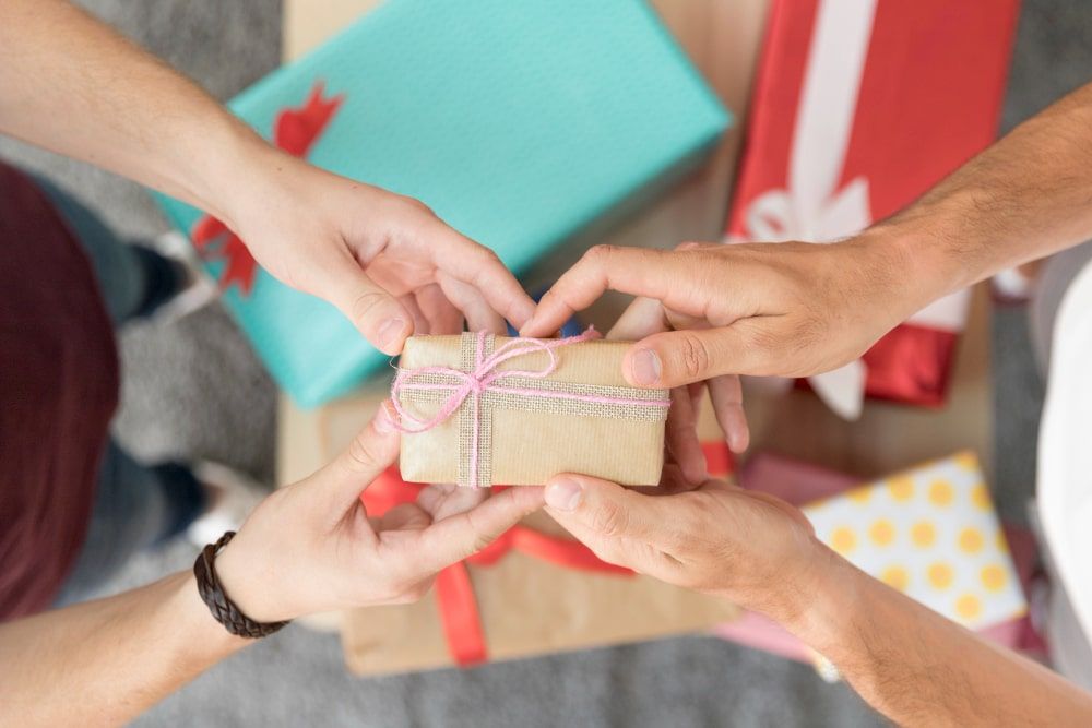 A couple grasping a pile of presents on top a pile of small client gifts