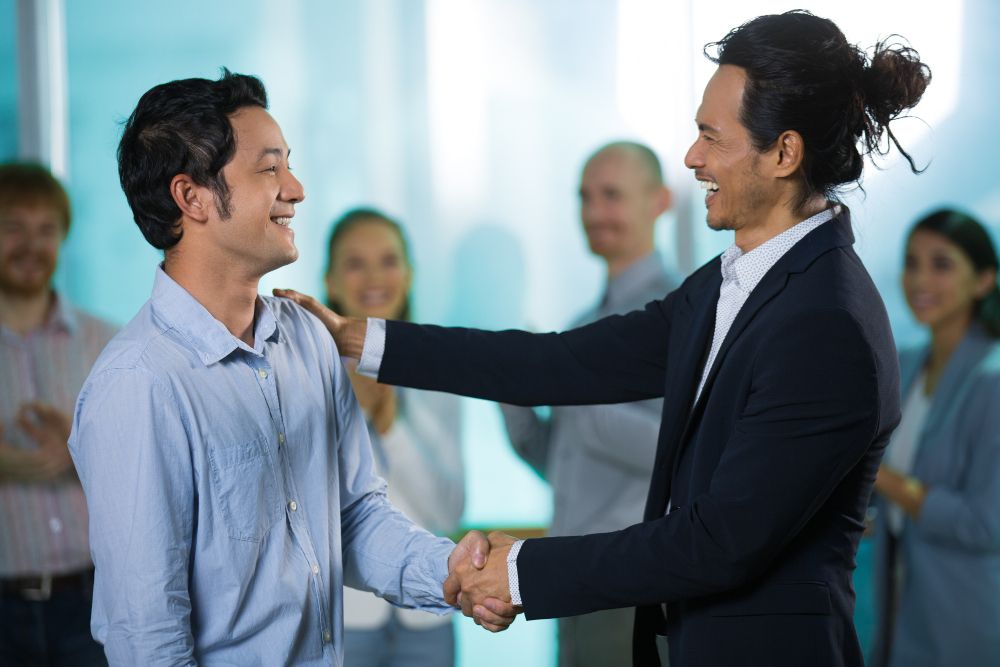 happy colleagues talking while shaking hands while talking about objectives of employee engagement