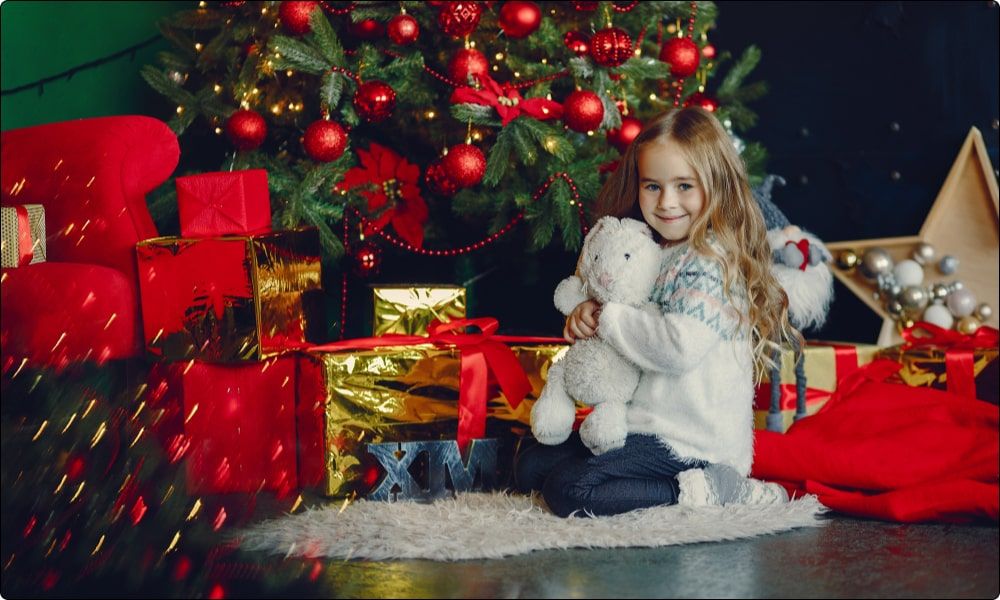 little girl by the christmas tree opening her christmas gifts