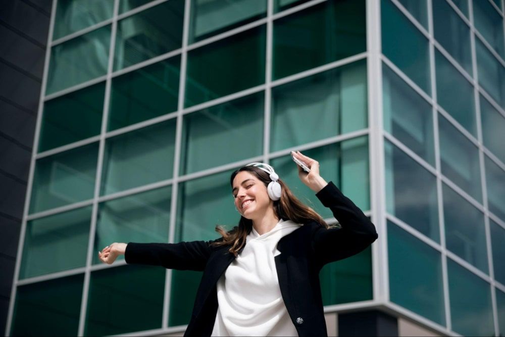 medium shot of a woman wearing headphones with a happy vibe outside of office building after giving away client referral gifts