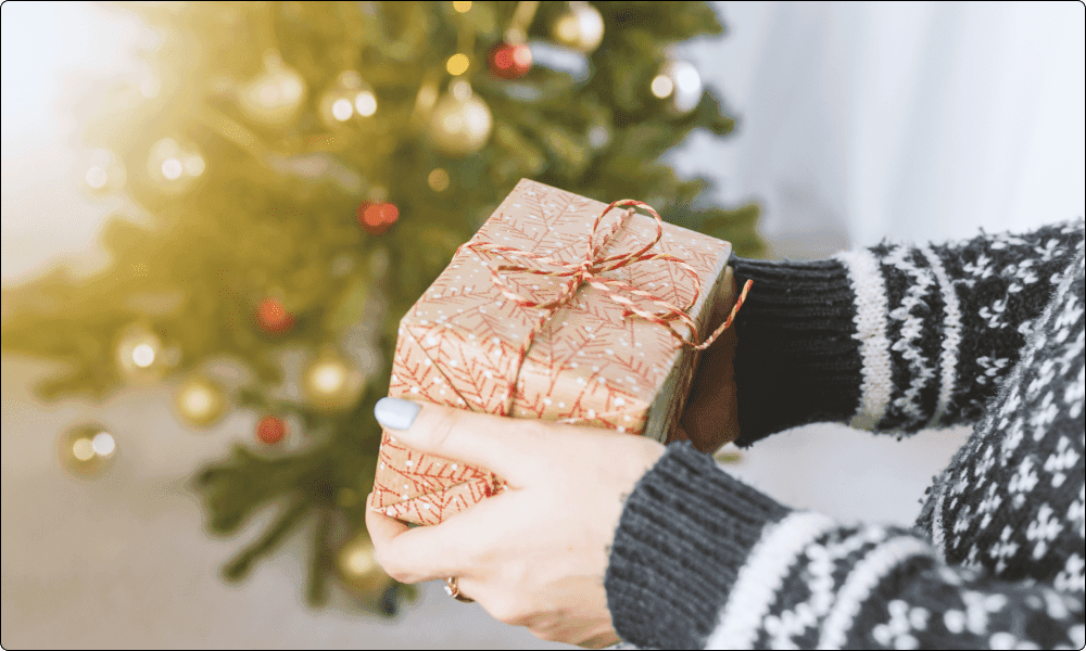 person giving someone a packaged gift with a christmas tree in the background