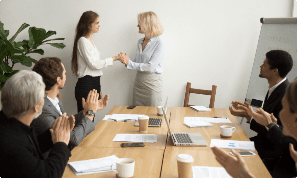 senior businesswoman thanking and recognizing female employee while team applauding