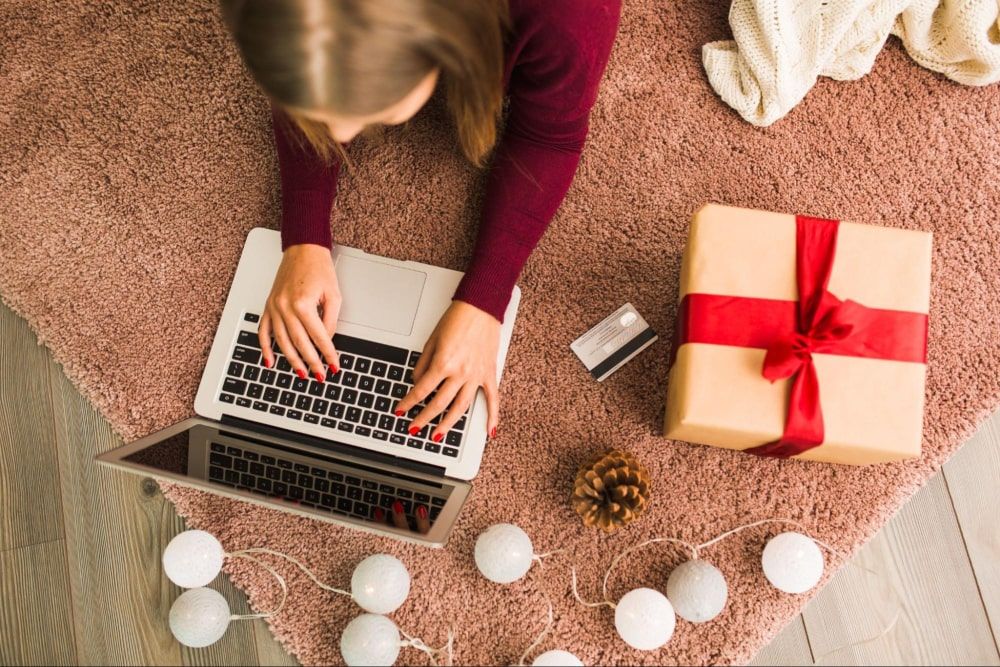 woman with a laptop surrounded by a credit card ready to shop due to Employee Gift Card Programs, present box, snag (a type of decorative fabric), and fairy lights